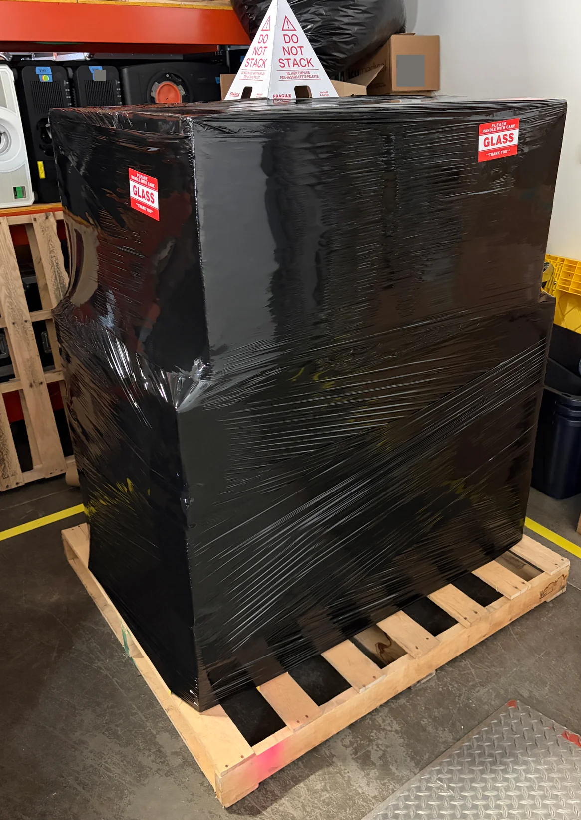 Black-wrapped freight pallet with handling labels and a do-not-stack cone.